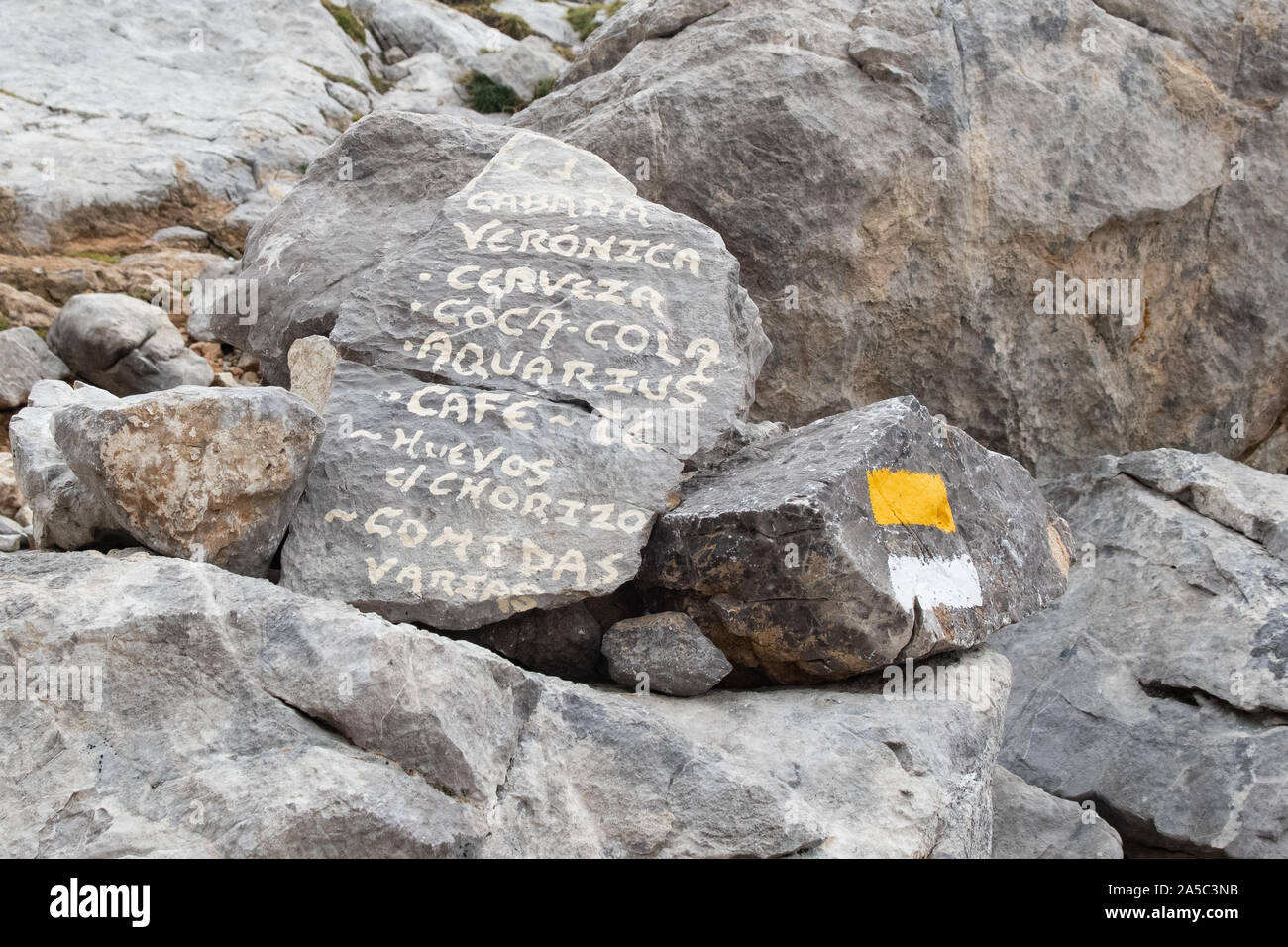 menu for Cabana Veronica mountain refuge painted onto a rock next to footpath marker, Picos de Europe, Spain, Europe Stock Photo