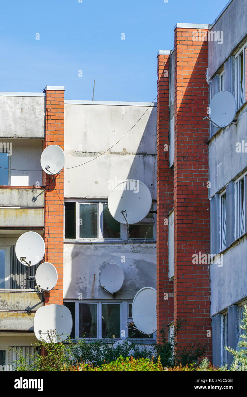 many white parabolic satellite antenna dishes hanged on wall of suburban perfab block of flats. Stock Photo