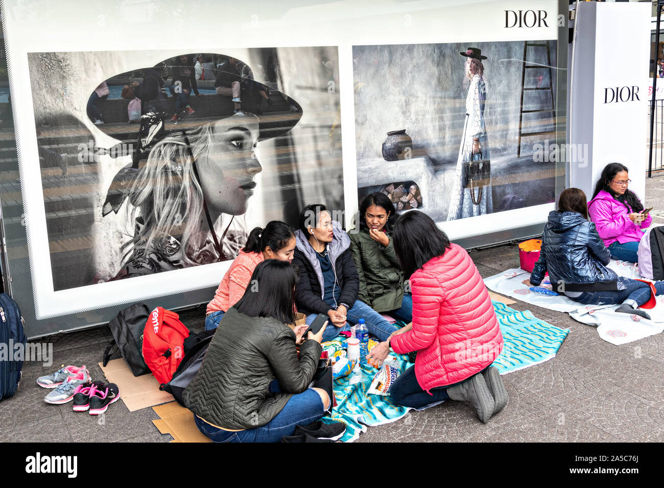Filipino domestic workers gather on their day-off in front of fashion advertisements in Central District, Hong Kong. Approximately 130,000 Filipino domestic servants work in Hong Kong and all have Sundays off. Stock Photo