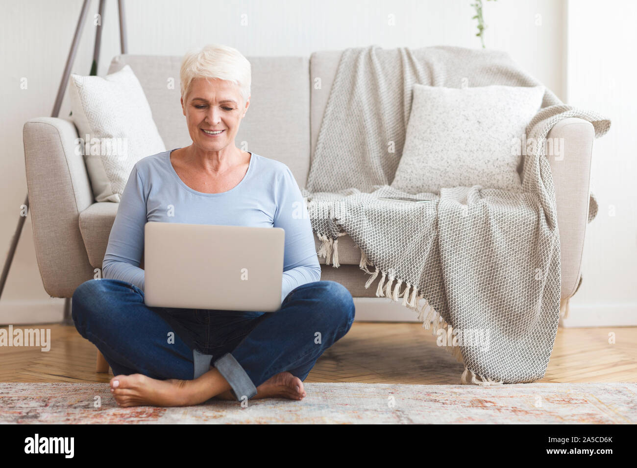 Resourceful mature woman sitting on floor and using laptop Stock Photo