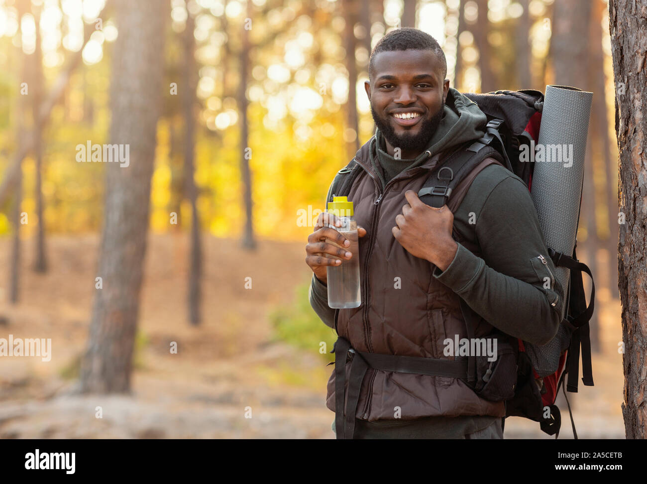 African man wearing backpack standing over forest background Stock Photo
