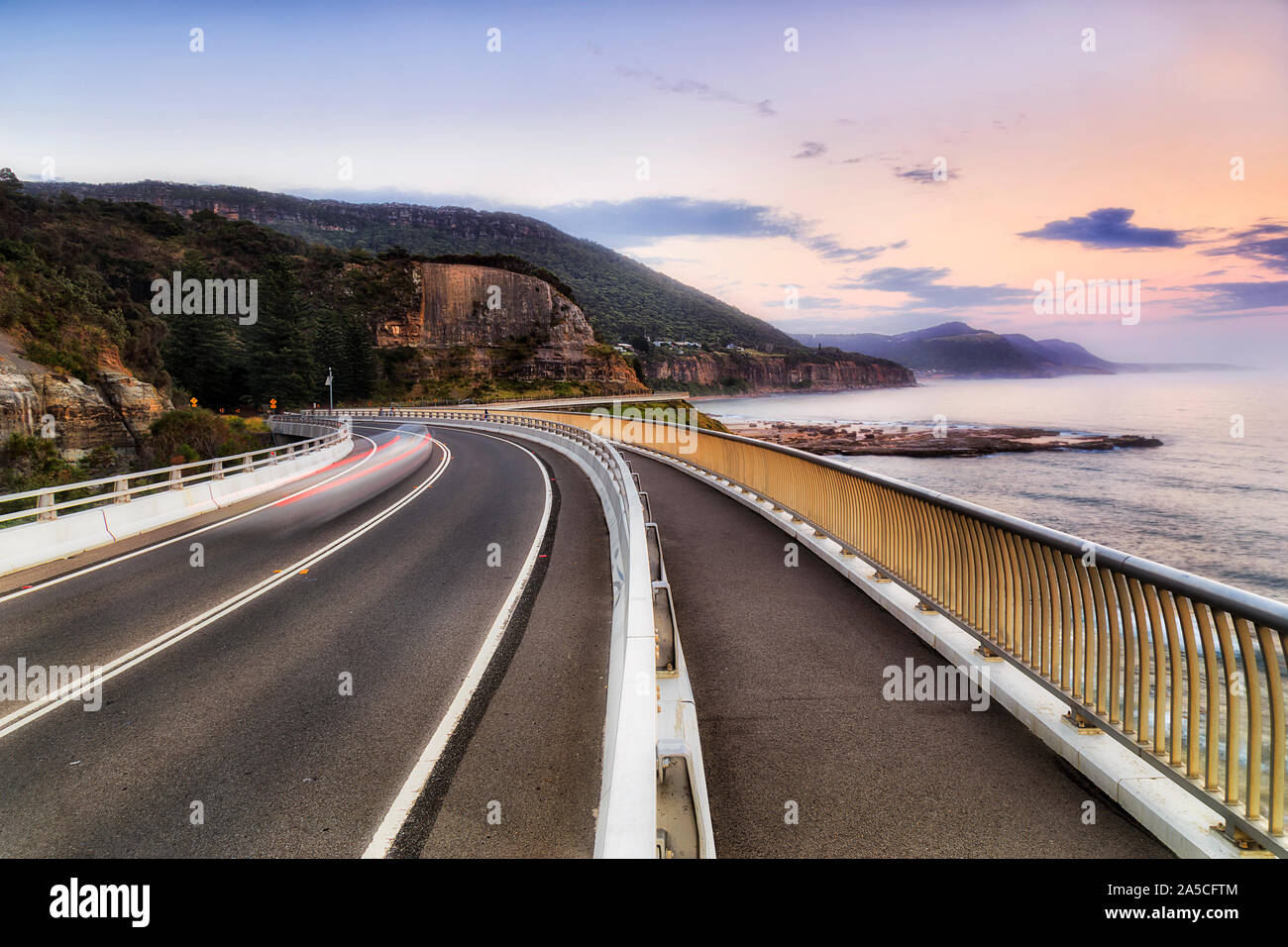 Grand Pacific Drive from Sydney to Wollongong via Sea Cliff Bridge facing north scenic coast of Australian Pacific ocean at sunrise with blurred passi Stock Photo
