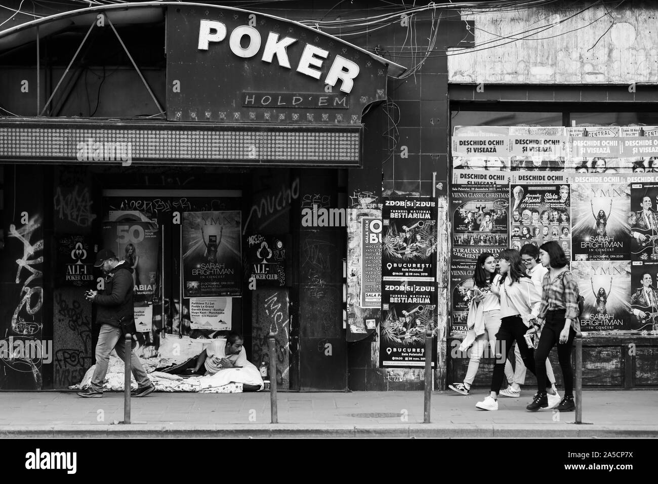 Bucharest, Romania - October 19, 2019: Homeless man on the sidewalk, laid down on a mat next to an abandoned building, with people walking by in downt Stock Photo