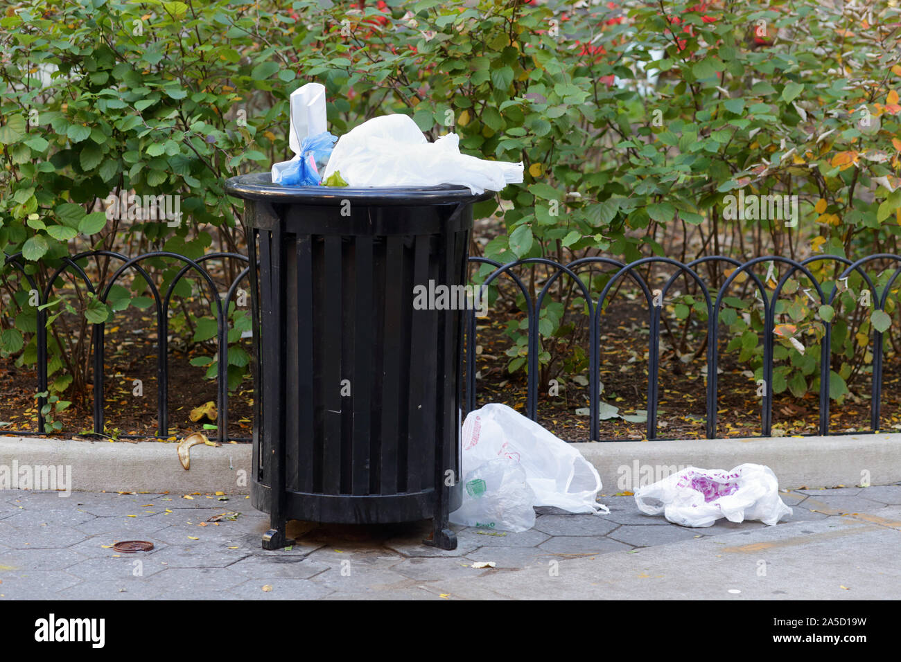 Single-use plastic bags loose on the ground near a garbage can. Stock Photo