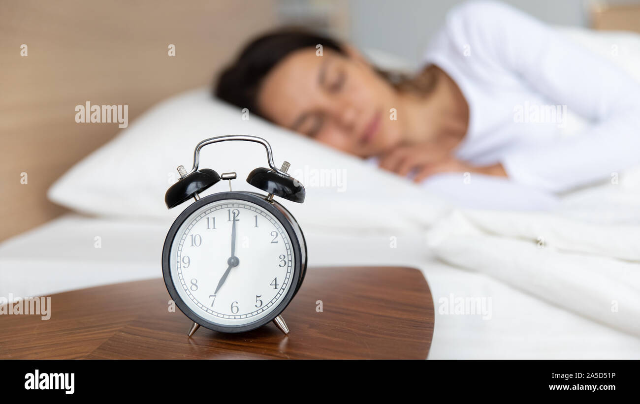 Close up mechanical alarm clock standing on bedside wooden table. Stock Photo