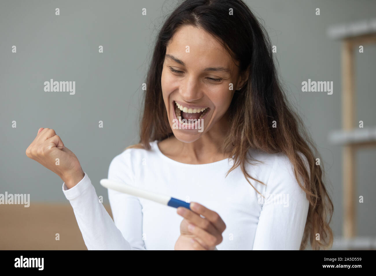 Overjoyed excited young mixed race lady holding pregnancy test Stock