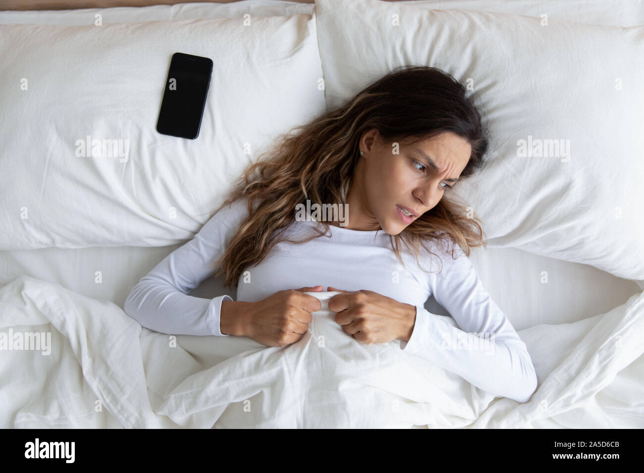 Irritated millennial mixed race woman waking up after cellphone alarm. Stock Photo