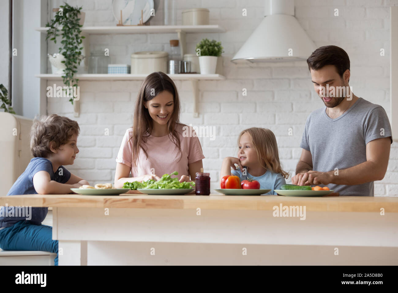 Happy parents with son and daughter preparing dinner, chatting Stock Photo