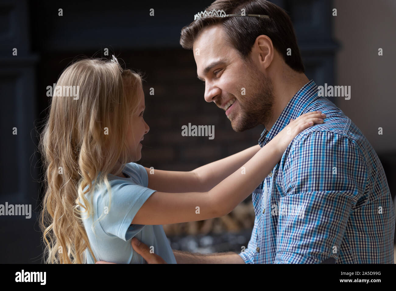Smiling father and daughter wearing crowns hugging at home Stock Photo