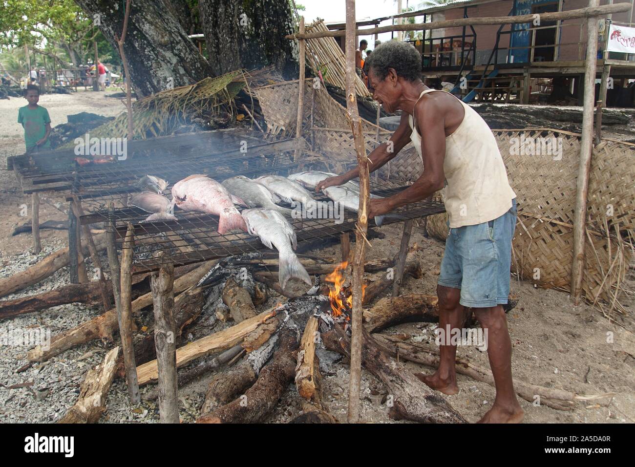Local Man smoking freshly caught Fish over a Charcoal Fire Stock Photo