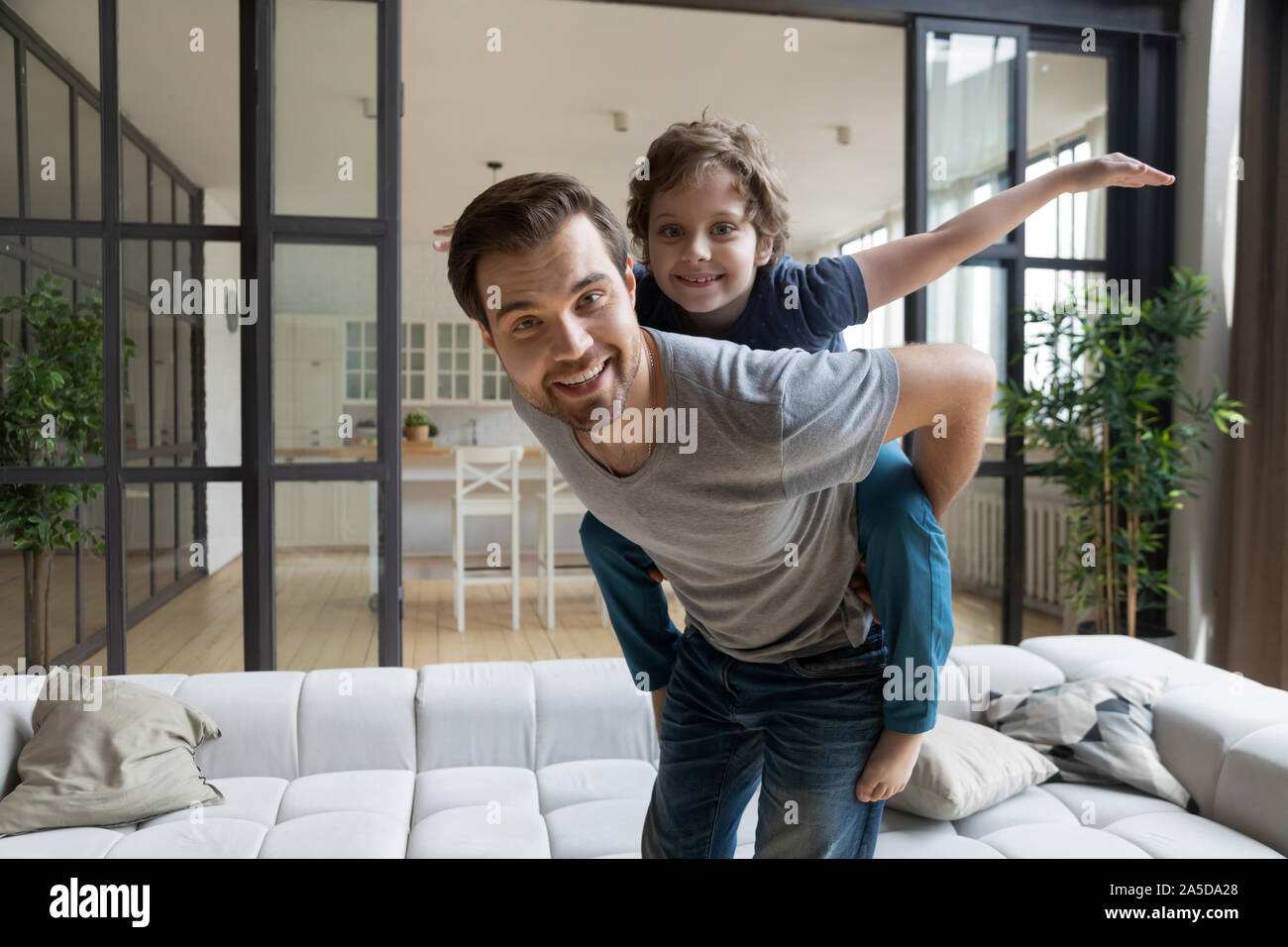 Portrait happy father piggybacking little son, having fun at home Stock Photo