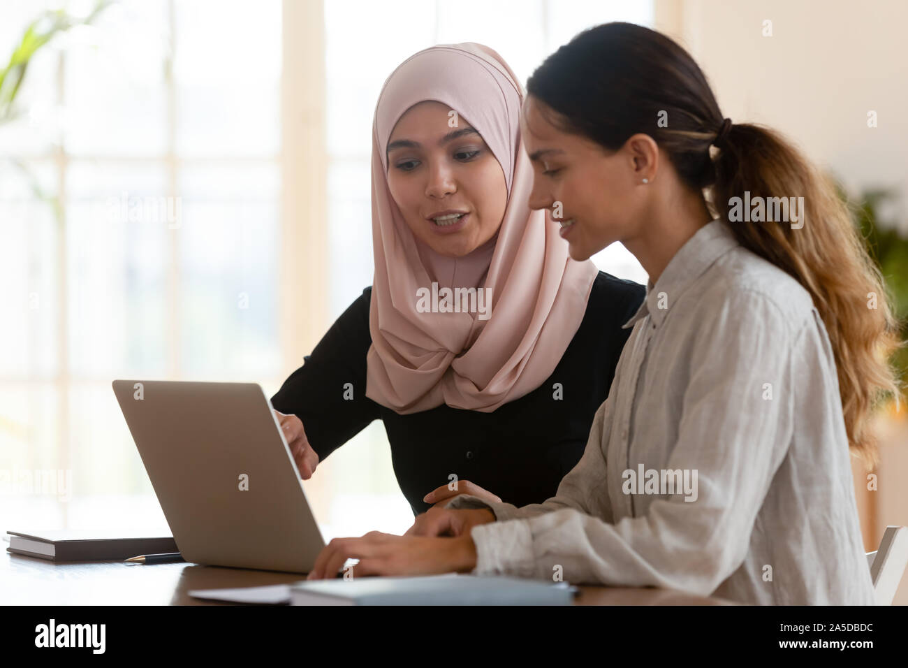 Asian muslim female mentor teaching caucasian intern explaining computer work Stock Photo