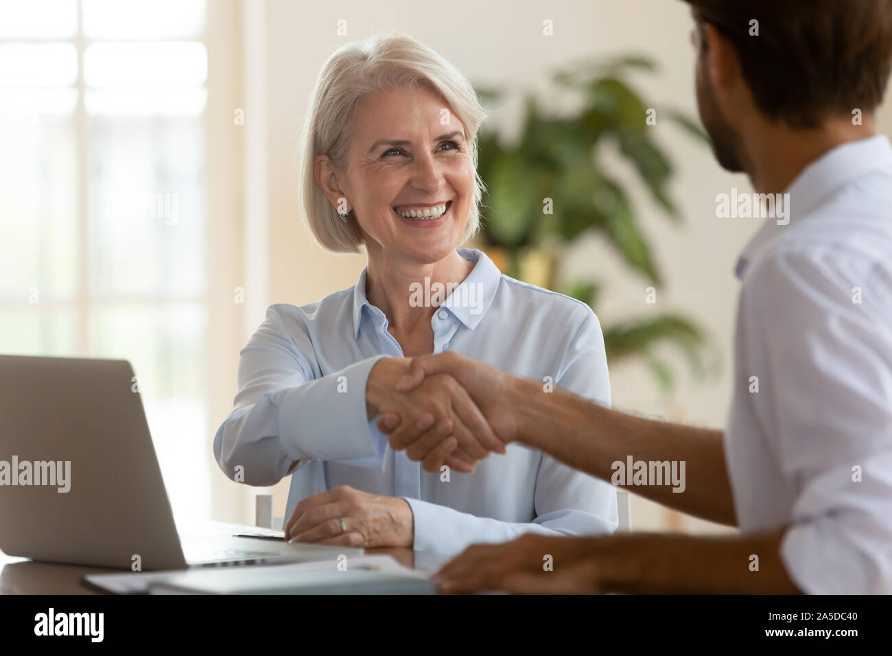 Smiling mature saleswoman handshake businessman client customer at business meeting Stock Photo