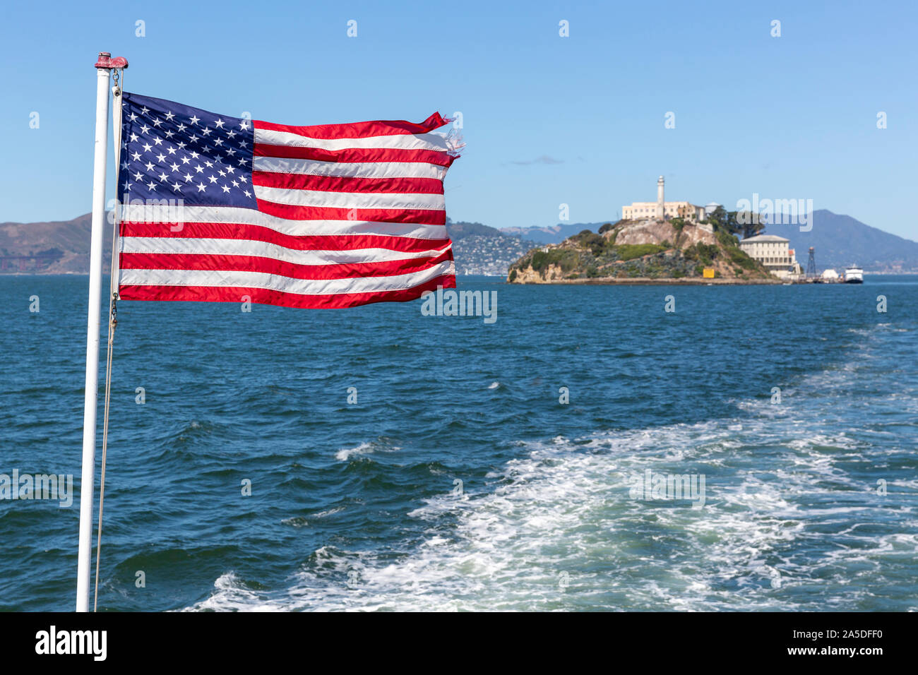 The Stars and Stripes flag flying from the back of a boat with Alcatraz Island out of focus behind. Stock Photo