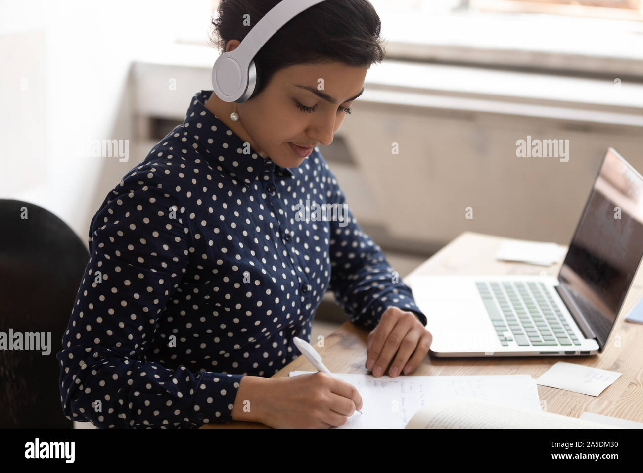 Indian ethnicity woman wearing headphones listens educational course studying online Stock Photo