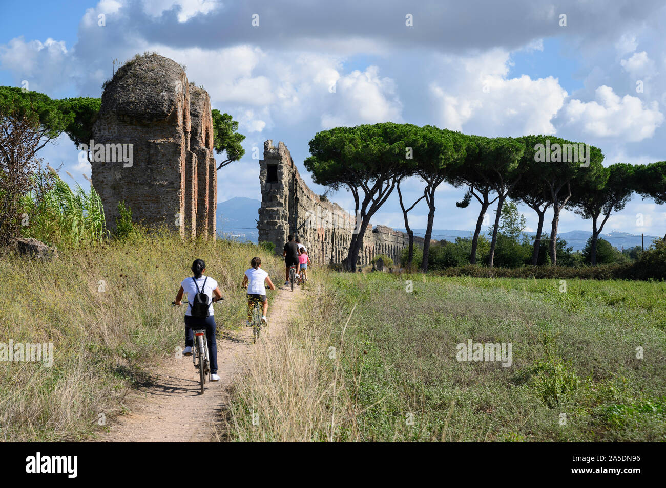 Rome. Italy. Parco degli Acquedotti, cyclists pass the ancient Roman aqueduct Aqua Claudia, begun by Emperor Caligula in 38 AD and finished by Emperor Stock Photo