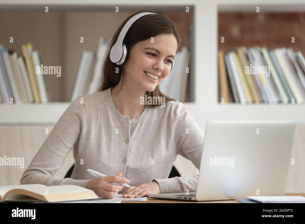 Girl in headphones look at pc screen noting studying indoors Stock Photo