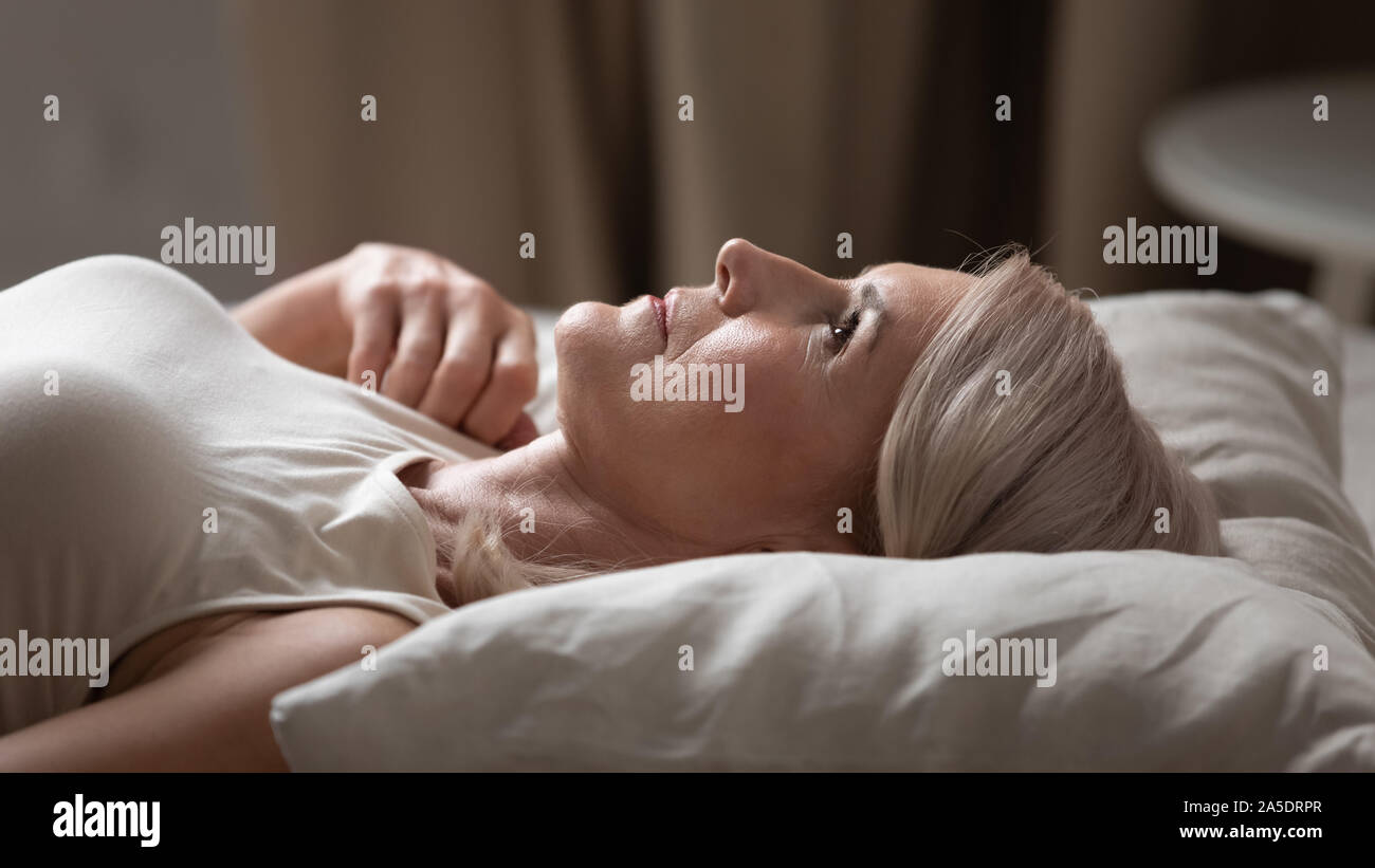 Disturbed mature older woman lying awake in uncomfortable bed Stock Photo