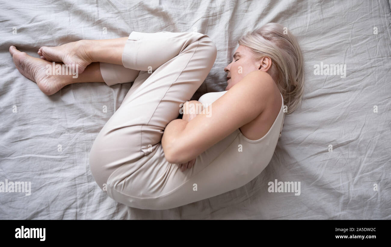 Depressed mature woman lying alone on bed in fetal position Stock Photo