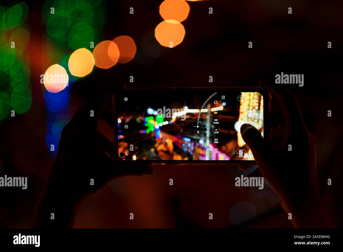 Person holding smart phone & capturing photo of festive decorations at night. Background image for street mobile photography, Diwali celebration. Stock Photo