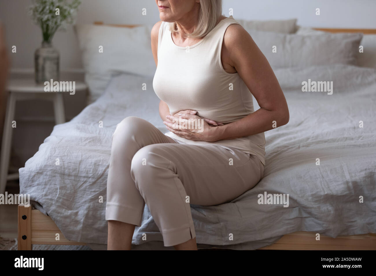Sick mature woman hold belly feel abdominal ache in bed Stock Photo