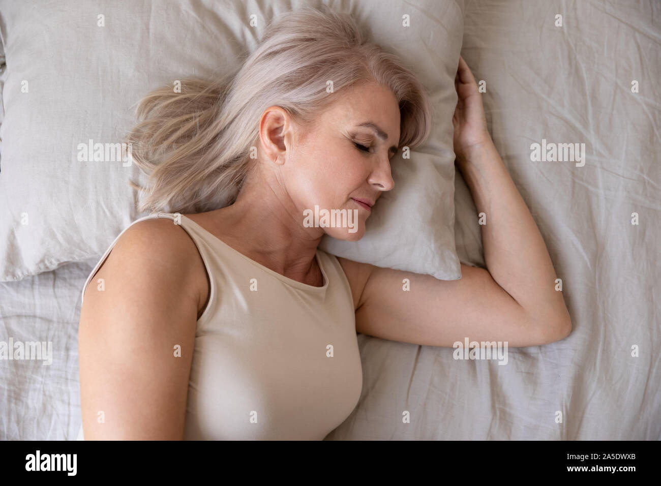 Peaceful healthy mature woman lying asleep in bed, top view Stock Photo