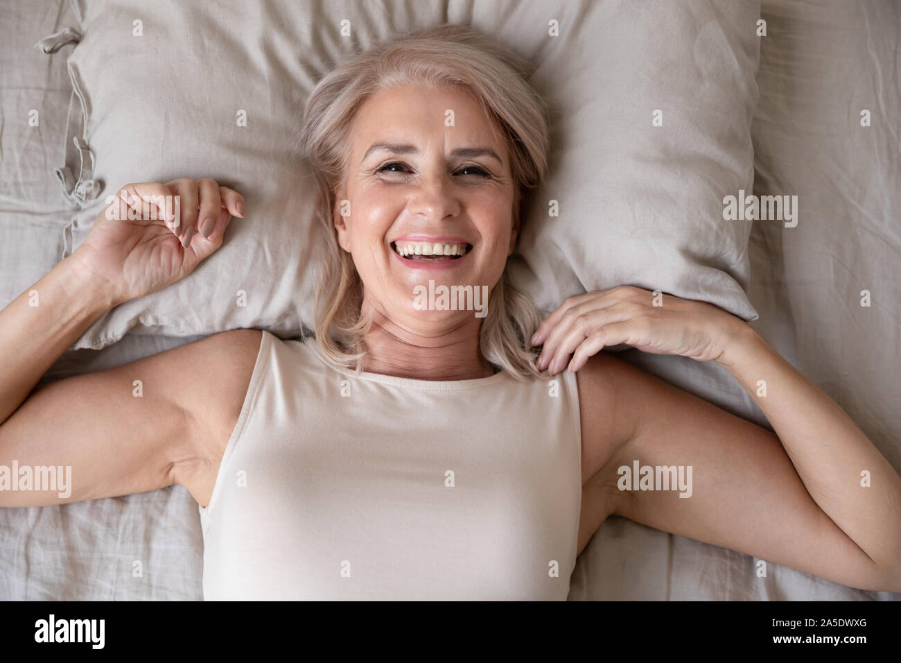 Happy older woman wake up in bed, top view Stock Photo
