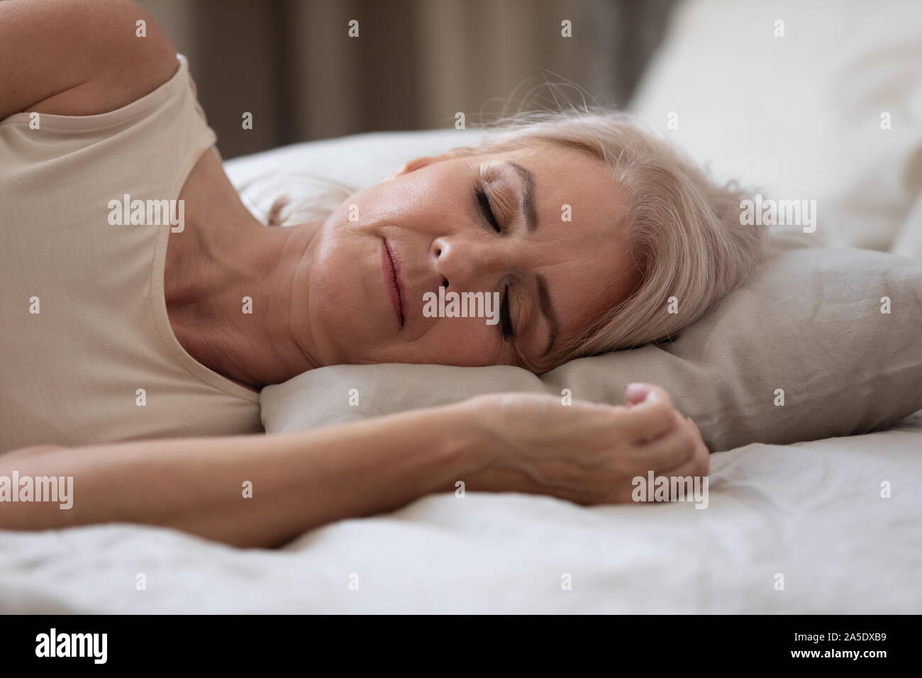 Calm serene older woman sleeping alone in bed, closeup view Stock Photo