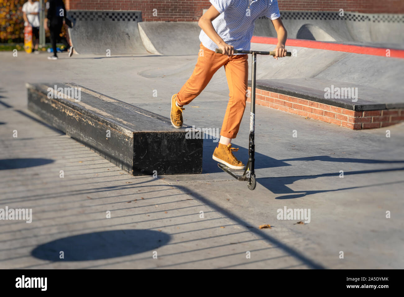 Feet in yellow sneakers and pants of teenager jumping a kick scooter at a skate park. Street culture of young Stock Photo