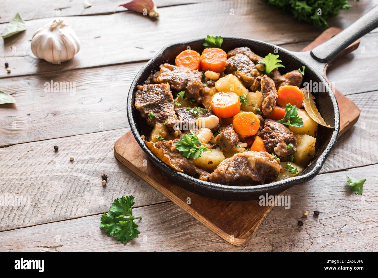 Beef meat stewed with potatoes, carrots and spices on wooden background, copy space. Homemade winter comfort food - slow cooked meat stew. Stock Photo