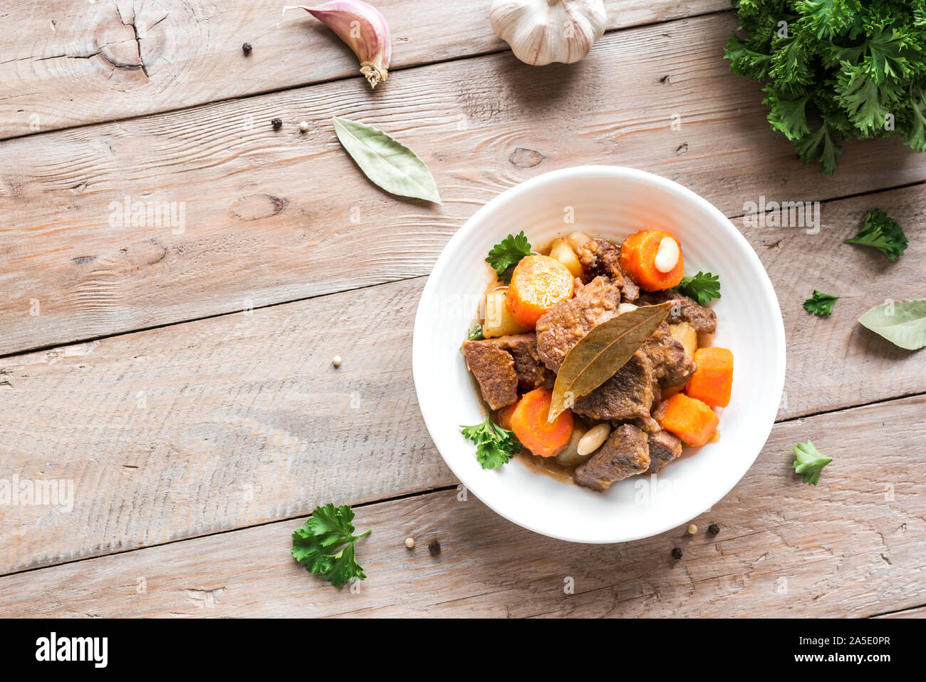 Beef meat stewed with potatoes, carrots and spices on wooden background, top view, copy space. Homemade winter comfort food - slow cooked meat stew. Stock Photo