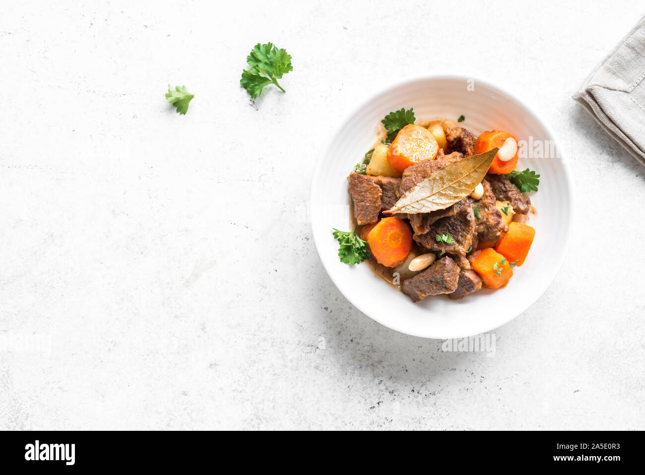 Beef meat stewed with potatoes, carrots and spices on white background, top view, copy space. Homemade winter comfort food - slow cooked meat stew. Stock Photo