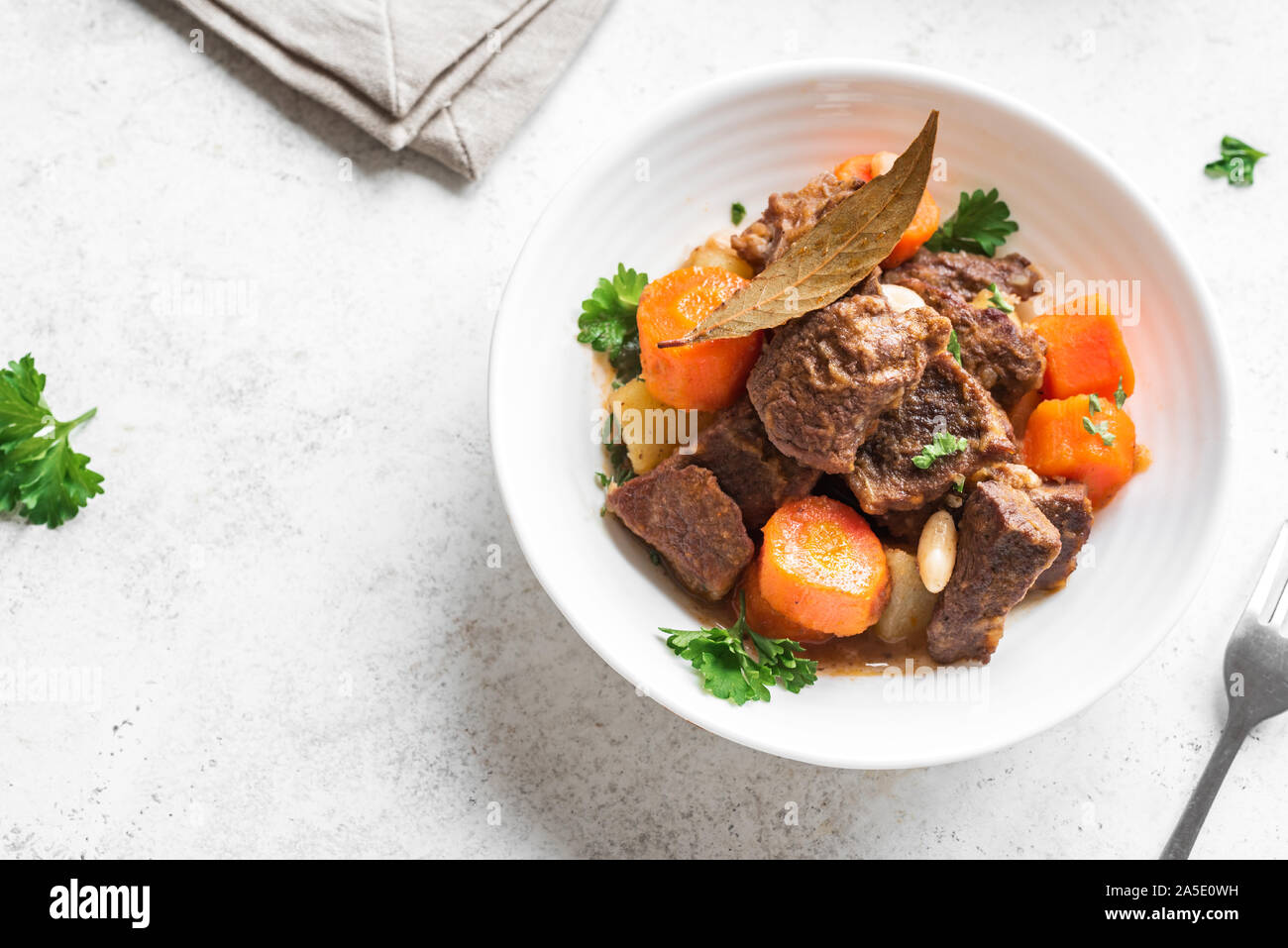 Beef meat stewed with potatoes, carrots and spices on white background, close up. Homemade winter comfort food - slow cooked meat stew. Stock Photo