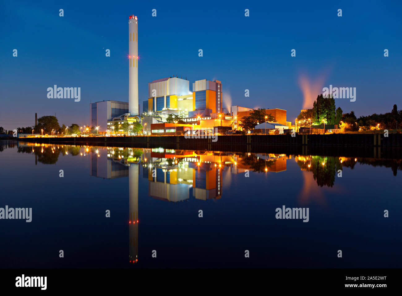 An incineration plant at a canal at blue hour in the night. Strong colors and very clear reflection. Stock Photo