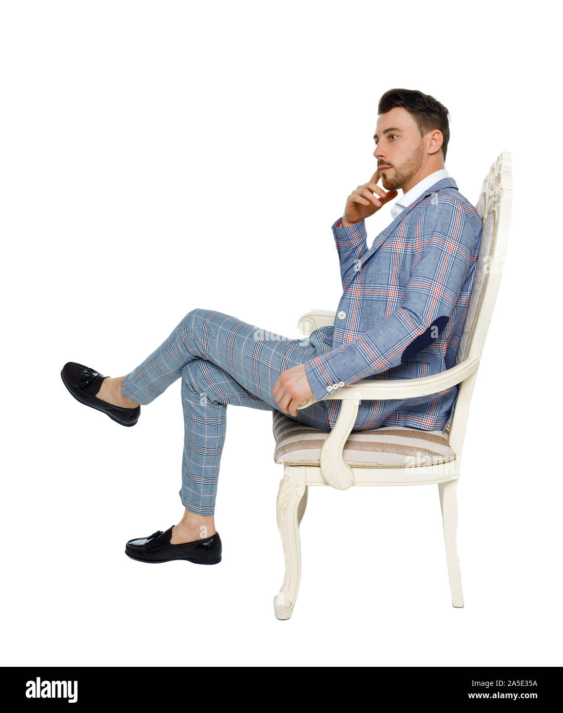 A man in a suit is sitting on an expensive chair. Side view of a guy in  stylish clothes on a chair. Isolated on white background. A stylish guy in  a l