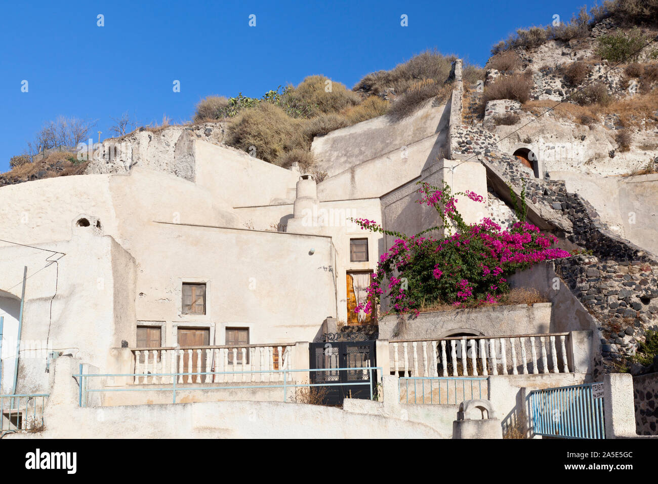 Houses built with caves into the pumice stone hills in little village Vothonas with blue sky. Santorini, Greece. Stock Photo