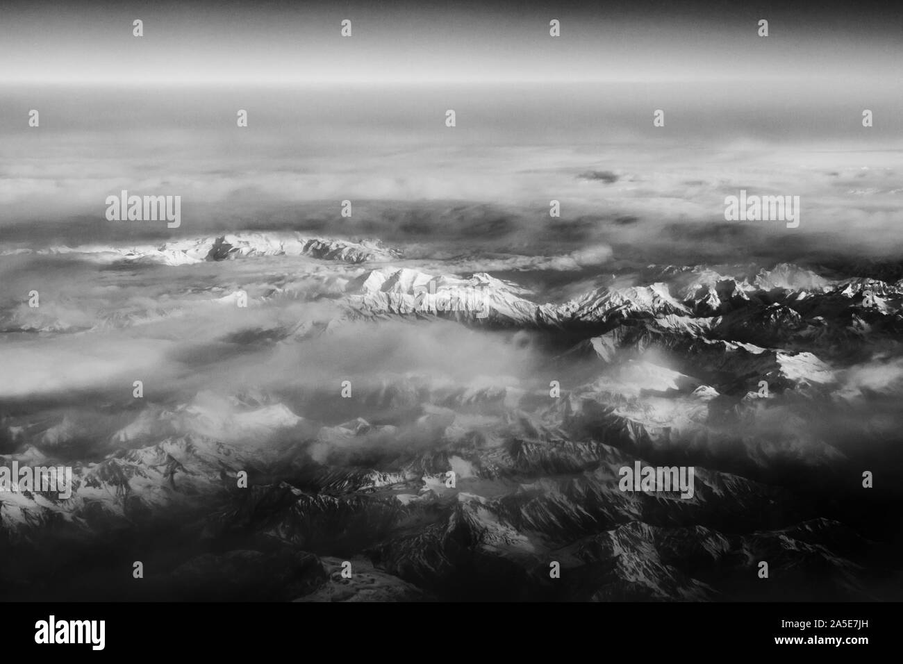 Aerial view from the plane on the panorama of the Alp mountains and hills ridge. Mountain peak of rocks covered by clouds and fog. View from above on Stock Photo