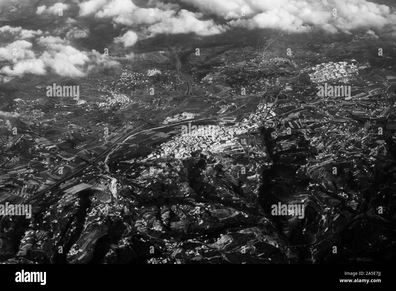 Aerial view from the plane on the panorama of the city through the clouds. View from above on the town near the mountains and hills ridge. View from a Stock Photo
