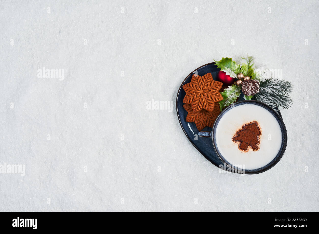 Gingerbread cookies with hot cocoa drink or cappuccino on snow. Top view of traditional Christmas gingerbread cookies with copy space. Stock Photo