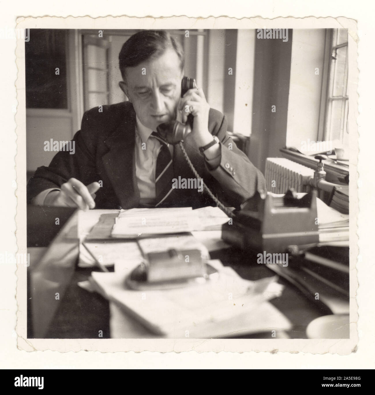 Photo of stressed older middle aged man working management, manager, managing / in office using telephone circa 1950's, U.K. Stock Photo