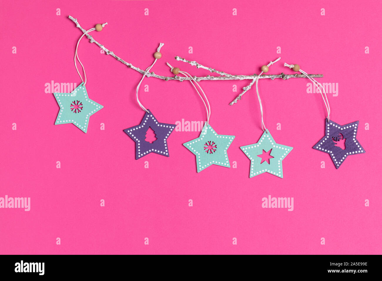 Xmas decorations. Christmas toys turquoise and purple painted wooden stars on white twig on bright pink background. Top view. Stock Photo