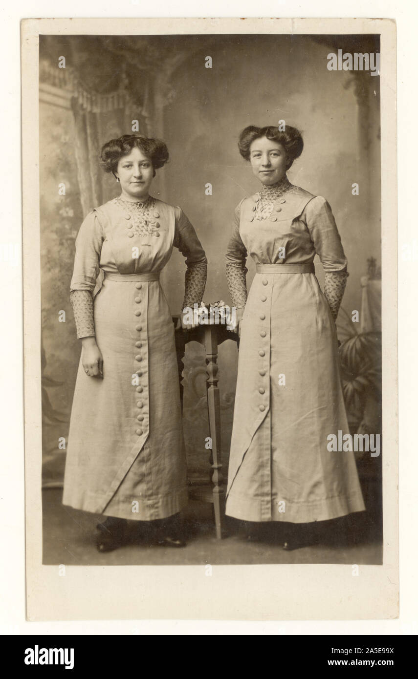 Original, clear early 1900's WW1 era postcard of attractive young women, sisters, like twins - siblings wearing matching button down dresses, blouses, long hemline, small waists. Interesting hairstyles, hair swept up on side. dated July 6 1914 on reverse, a poignant photograph taken days before the outbreak of the first world war, U.K. Stock Photo