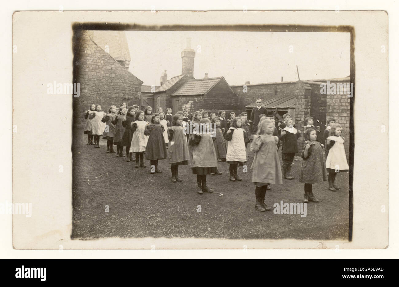 Original charming early 1900's photo of Victorian schoolchildren girls and boys, Victorian schoolgirl schoolgirls, Victorian schoolboy schoolboys, Victorian children, wearing smart clothes, exercising outside, in school yard, girls wear pinafores, teacher monitors, monitoring, circa 1905, U.K. Stock Photo