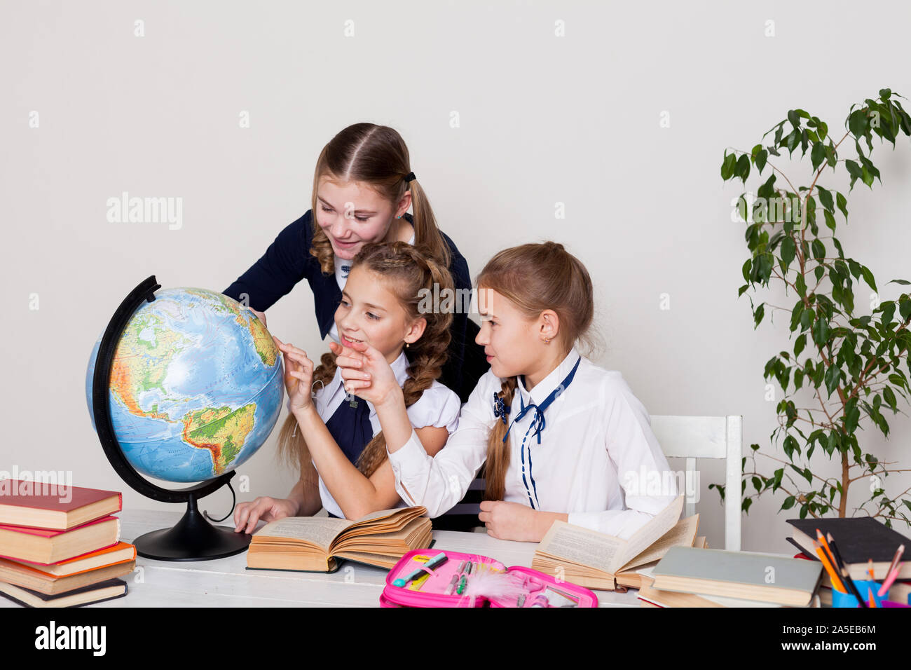 three girls with books and a globe in class at the desk at school Stock ...