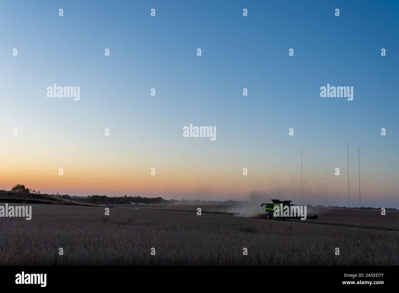 A combine works in a field at dusk with the Alleman towers in the