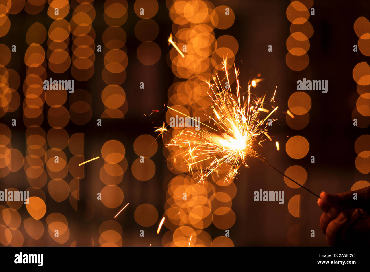 Diwali holiday greetings card, postcard. A young woman holding lighted fireworks with bright golden Christmas bokeh lights. Background image for Diwal Stock Photo