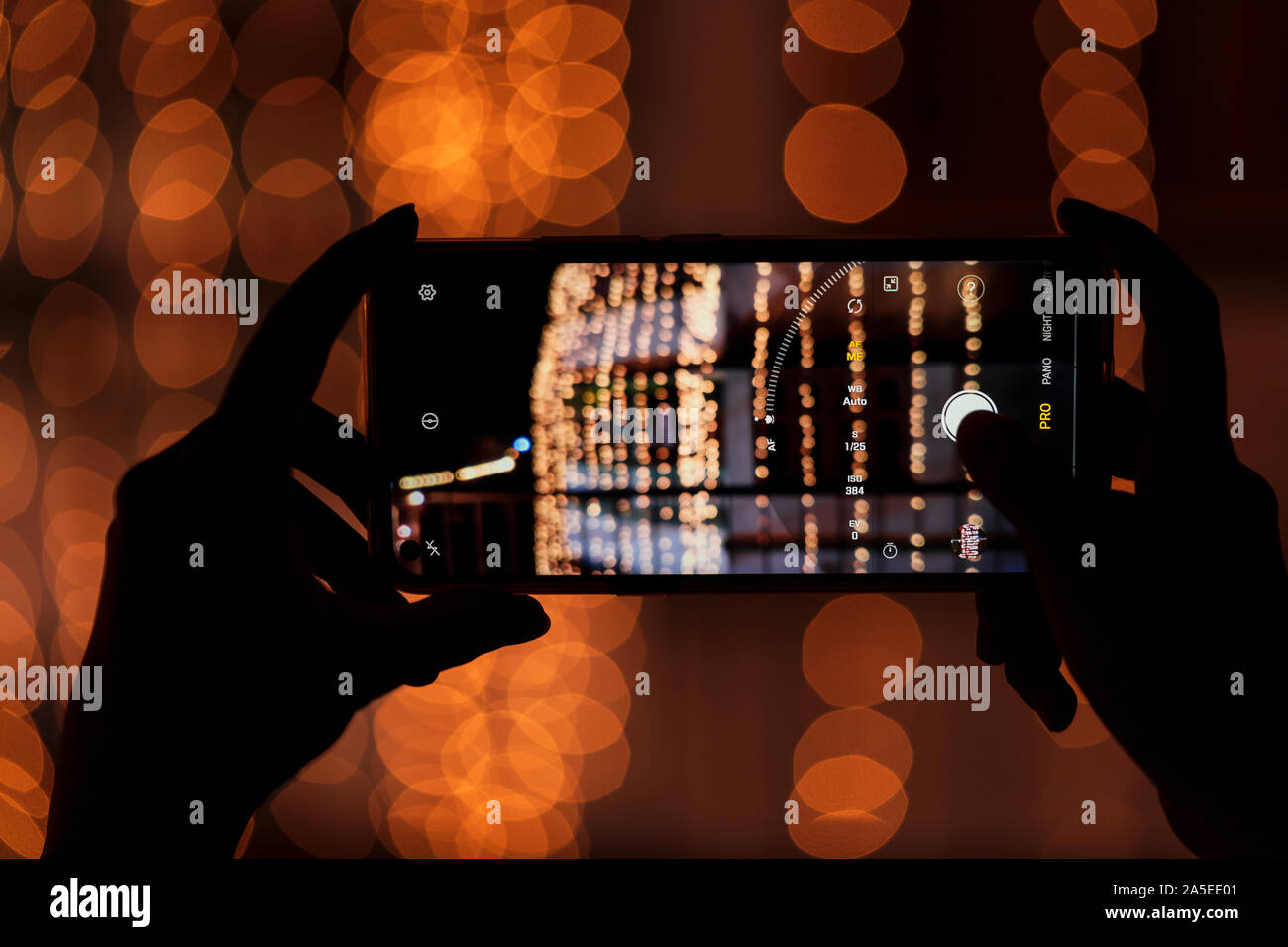 Person holding smart phone & capturing photo of festive decorations at night. Background image for Diwali festival, street mobile photography. Stock Photo