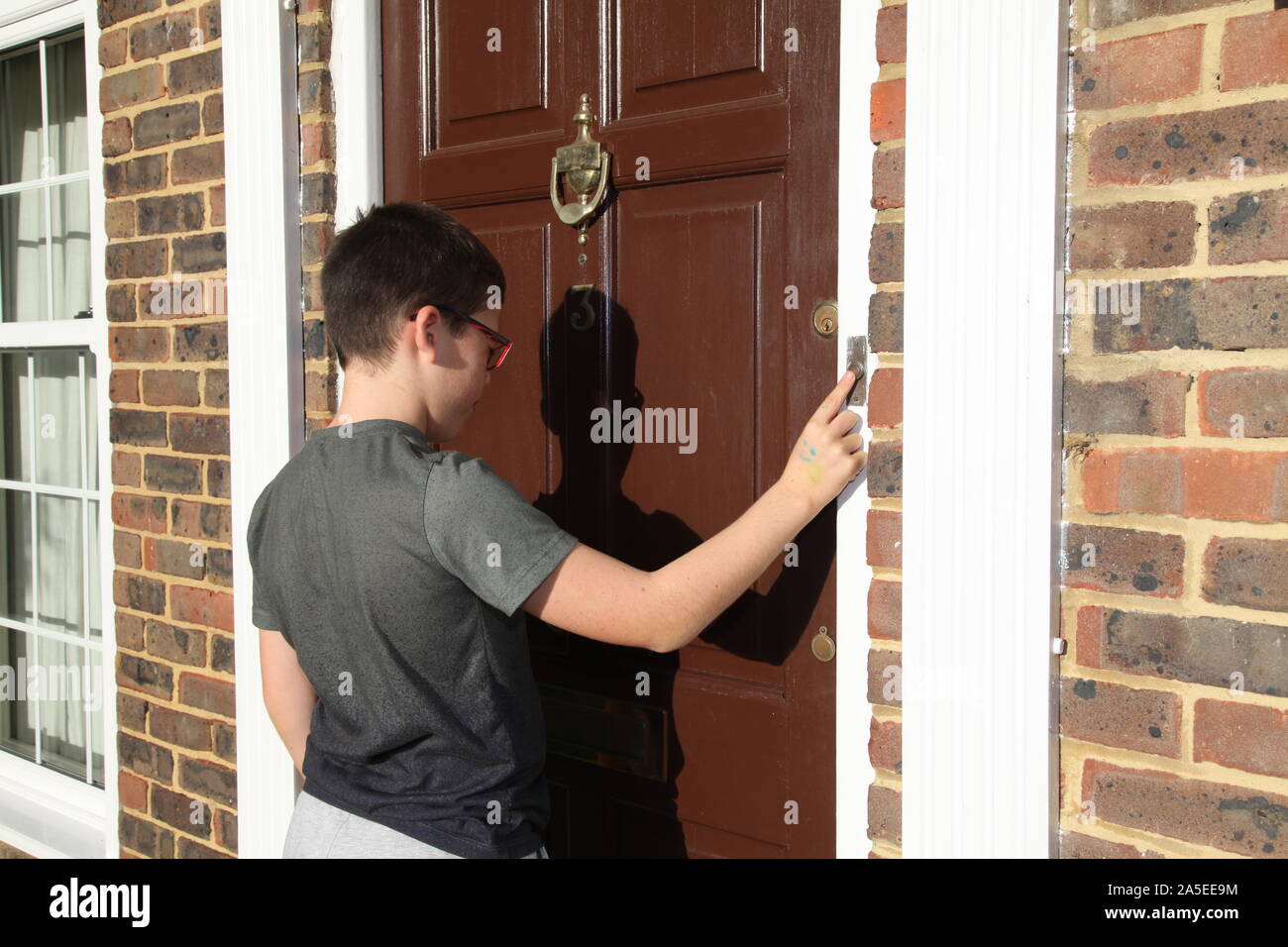 Child ringing doorbell on front door of house, number 3, wearing glasses, brown door, Georgian house, UK Stock Photo