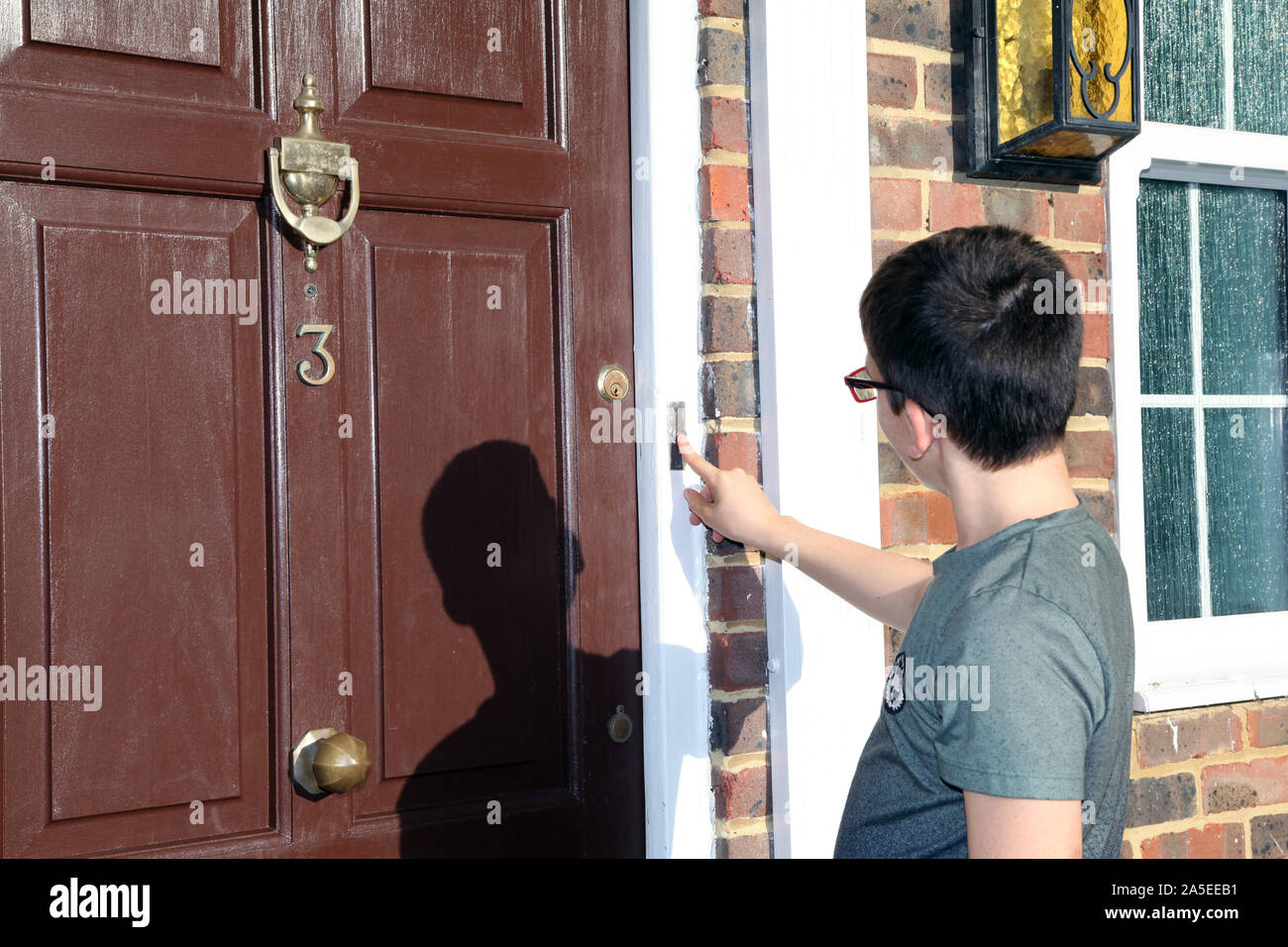 Child ringing doorbell on front door, number 3, wearing glasses, brown door, Georgian house, UK Stock Photo