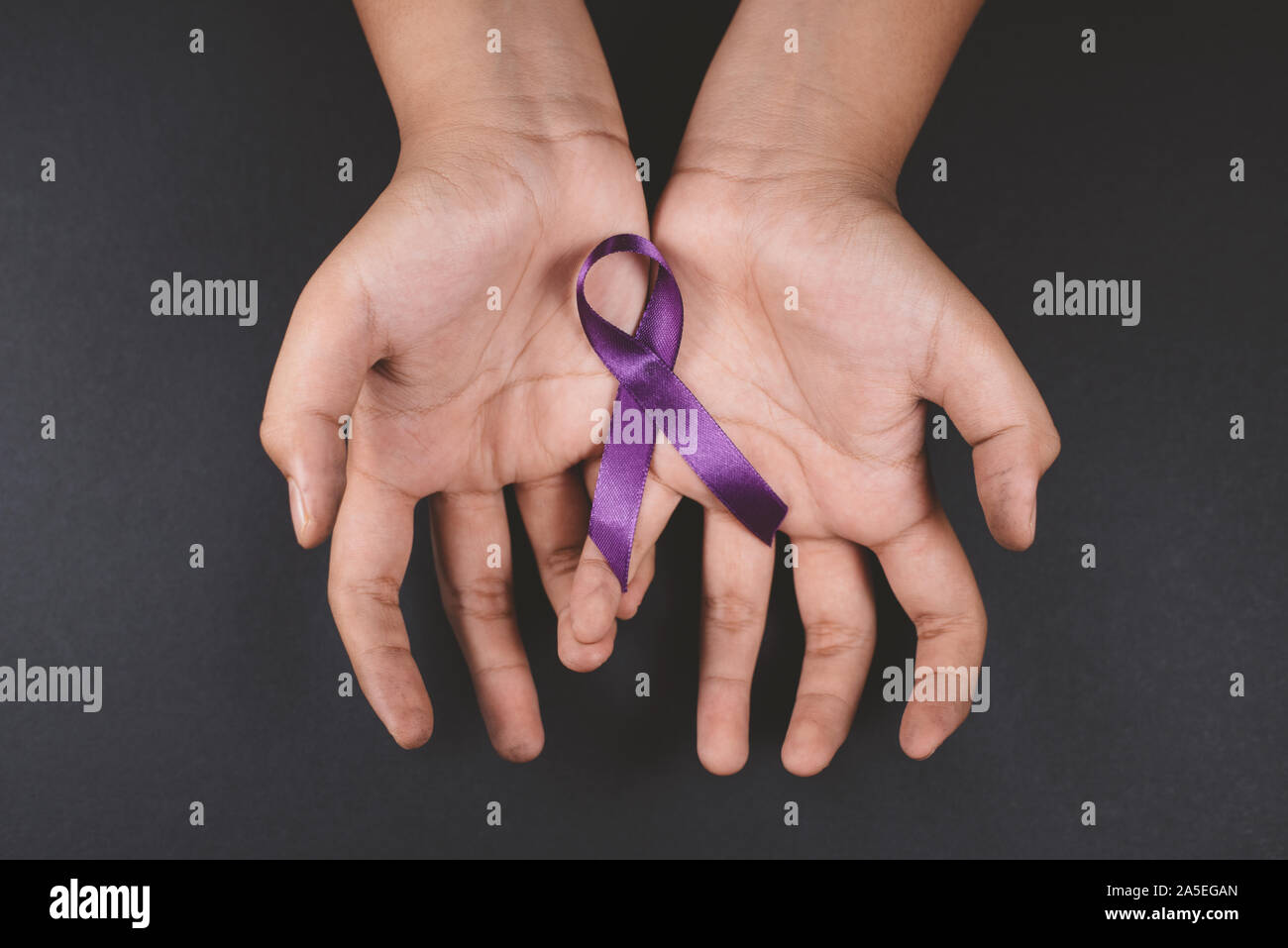 Purple ribbon on cramps hand against black background Stock Photo